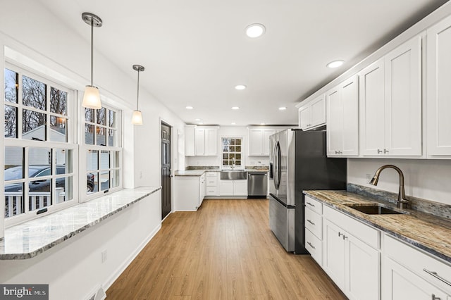 kitchen with sink, white cabinetry, decorative light fixtures, appliances with stainless steel finishes, and light hardwood / wood-style floors