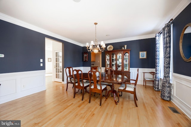 dining area with light wood-type flooring, an inviting chandelier, and ornamental molding