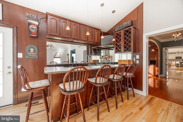 bar with light hardwood / wood-style flooring, vaulted ceiling, decorative light fixtures, ceiling fan with notable chandelier, and ornamental molding