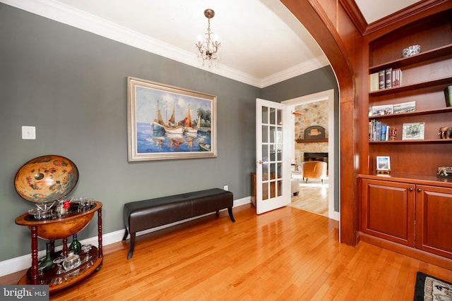 living area with crown molding, light hardwood / wood-style flooring, built in features, a chandelier, and a stone fireplace