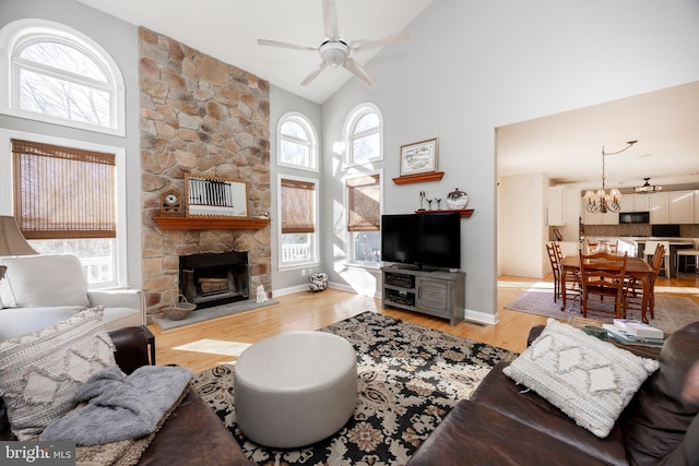 living room featuring a fireplace, ceiling fan with notable chandelier, high vaulted ceiling, and light hardwood / wood-style flooring