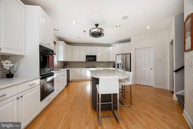 kitchen featuring a breakfast bar, white cabinetry, a kitchen island, and black appliances