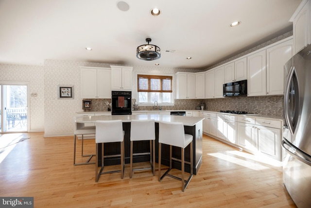 kitchen with white cabinets, light hardwood / wood-style flooring, a kitchen island, and black appliances