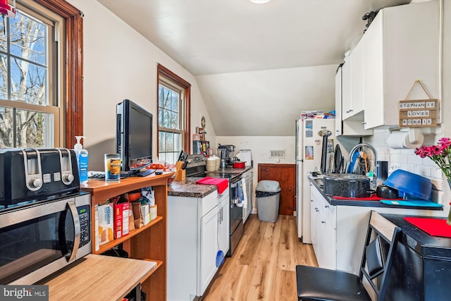 kitchen with light wood-type flooring, tasteful backsplash, stainless steel appliances, white cabinets, and lofted ceiling