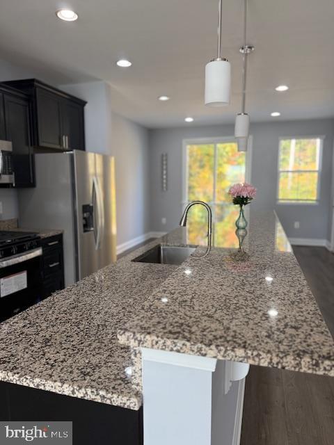 kitchen featuring a large island with sink, light stone counters, black electric range oven, and hanging light fixtures