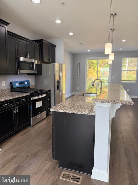 kitchen featuring a kitchen island with sink, hardwood / wood-style floors, decorative light fixtures, and appliances with stainless steel finishes