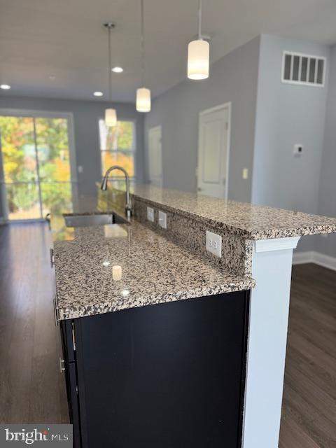 kitchen featuring light stone counters, dark wood-type flooring, sink, decorative light fixtures, and an island with sink