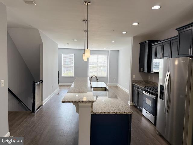 kitchen featuring sink, light stone countertops, an island with sink, appliances with stainless steel finishes, and decorative light fixtures