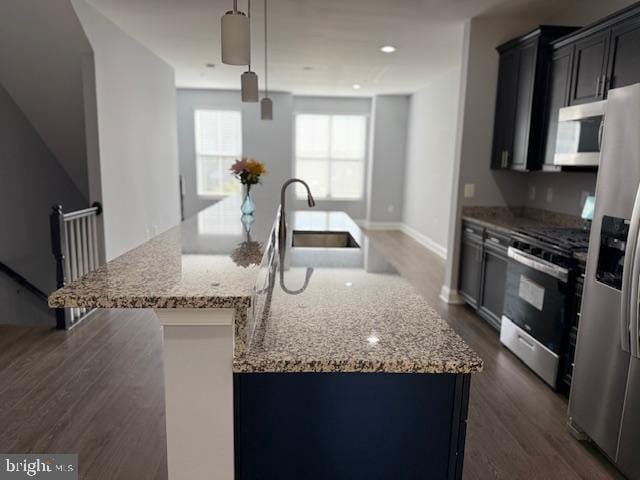 kitchen featuring sink, hanging light fixtures, light stone countertops, an island with sink, and stainless steel appliances