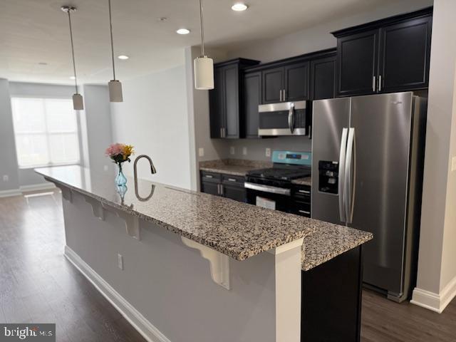 kitchen with light stone counters, a breakfast bar, stainless steel appliances, decorative light fixtures, and an island with sink