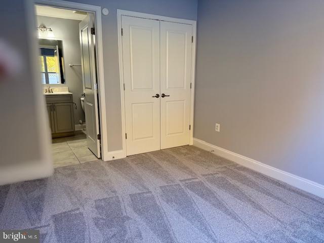 unfurnished bedroom with ensuite bathroom, a closet, and light carpet