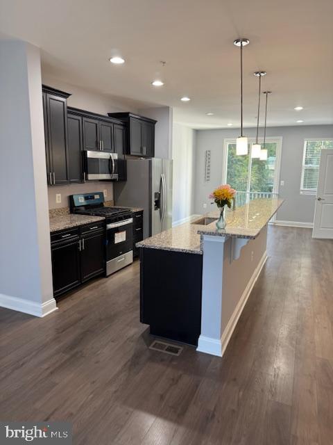 kitchen with hanging light fixtures, an island with sink, dark hardwood / wood-style flooring, a breakfast bar area, and stainless steel appliances