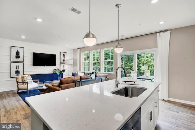 kitchen with white cabinetry, sink, light stone counters, decorative light fixtures, and a kitchen island with sink