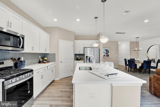 kitchen with sink, hanging light fixtures, appliances with stainless steel finishes, and an island with sink