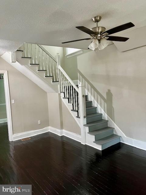 stairway with ceiling fan, wood-type flooring, and a textured ceiling