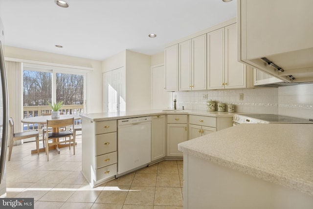 kitchen featuring backsplash, light tile patterned floors, white dishwasher, kitchen peninsula, and cream cabinets