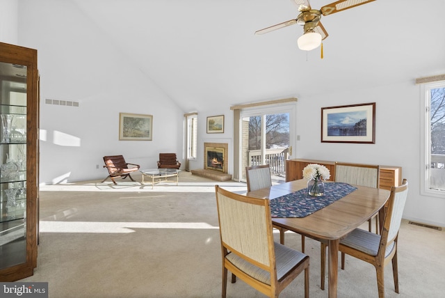 dining space featuring ceiling fan, light colored carpet, a fireplace, and high vaulted ceiling