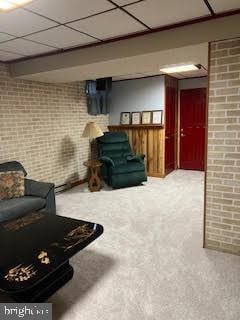 living room featuring a paneled ceiling, carpet, and brick wall