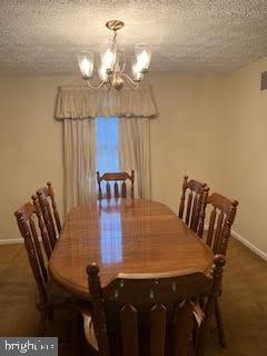 dining space featuring a chandelier, a textured ceiling, and dark colored carpet