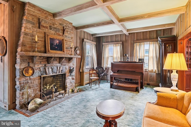 living area featuring beam ceiling, a stone fireplace, wooden walls, and carpet floors