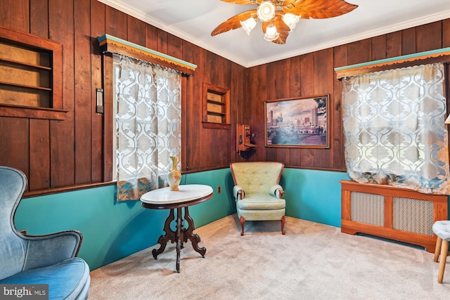 sitting room with wooden walls, light colored carpet, ceiling fan, and ornamental molding