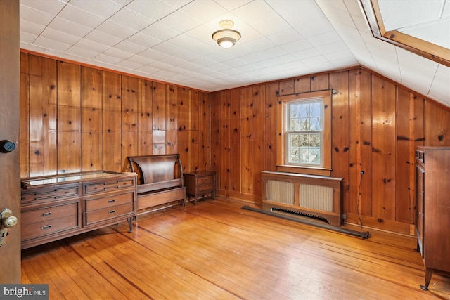 interior space with wooden walls, radiator heating unit, light hardwood / wood-style floors, and lofted ceiling