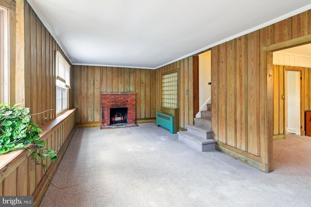 unfurnished living room featuring radiator, a brick fireplace, wood walls, light colored carpet, and ornamental molding