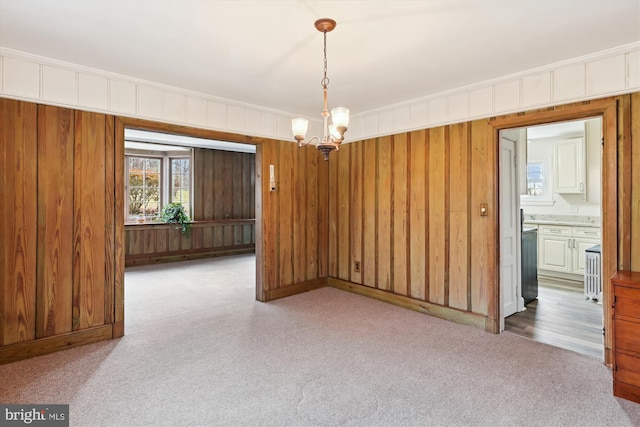 empty room with carpet flooring, wooden walls, ornamental molding, and an inviting chandelier