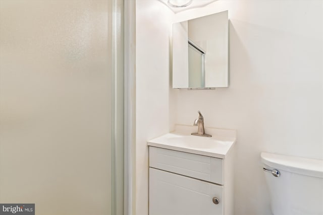 bathroom featuring a shower with door, vanity, and toilet