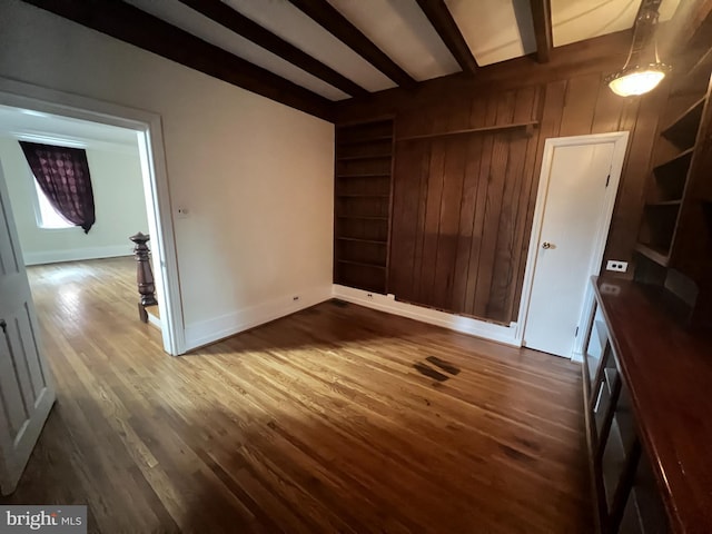 unfurnished bedroom featuring beamed ceiling, dark hardwood / wood-style floors, and wood walls