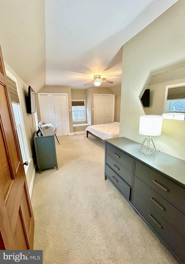 bedroom with two closets, light colored carpet, and ceiling fan