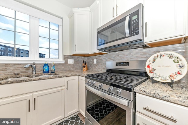 kitchen with decorative backsplash, light stone counters, white cabinets, and appliances with stainless steel finishes