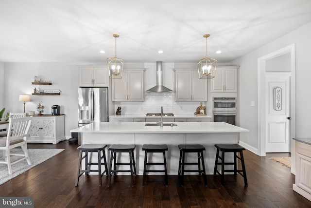 kitchen with a breakfast bar, a center island with sink, wall chimney range hood, appliances with stainless steel finishes, and decorative light fixtures