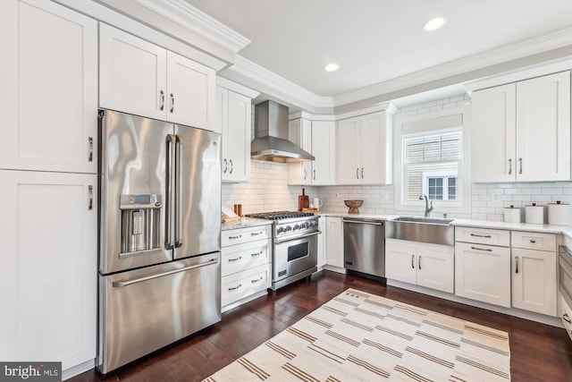 kitchen featuring high quality appliances, wall chimney range hood, sink, tasteful backsplash, and white cabinetry