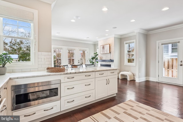 kitchen with dark hardwood / wood-style floors, ornamental molding, tasteful backsplash, light stone counters, and white cabinetry