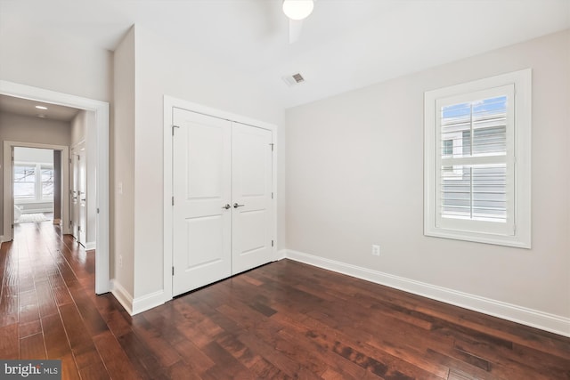 unfurnished bedroom featuring multiple windows, a closet, and dark hardwood / wood-style flooring