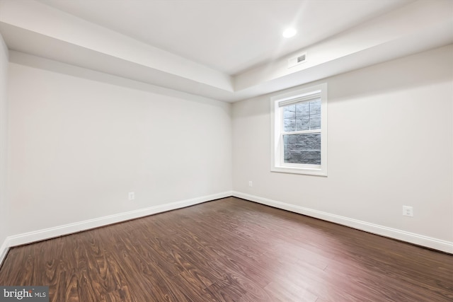 spare room with a raised ceiling and dark wood-type flooring