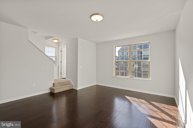 empty room with a wealth of natural light and dark hardwood / wood-style flooring