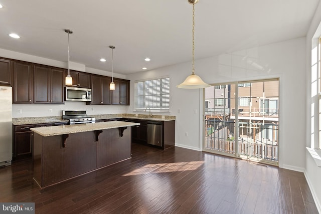 kitchen featuring a kitchen bar, light stone countertops, stainless steel appliances, a kitchen island, and hanging light fixtures