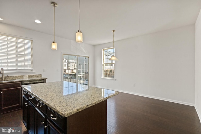 kitchen featuring sink, dark wood-type flooring, hanging light fixtures, light stone counters, and a kitchen island