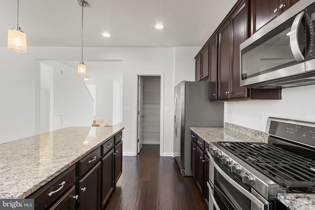 kitchen with appliances with stainless steel finishes, dark hardwood / wood-style flooring, light stone counters, and hanging light fixtures