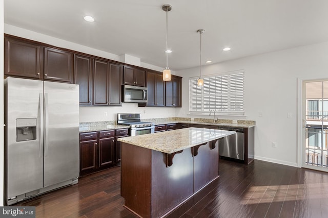 kitchen with stainless steel appliances, light stone counters, pendant lighting, a breakfast bar, and a kitchen island