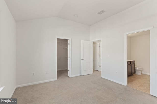 unfurnished bedroom with lofted ceiling, ensuite bath, a spacious closet, light colored carpet, and a closet