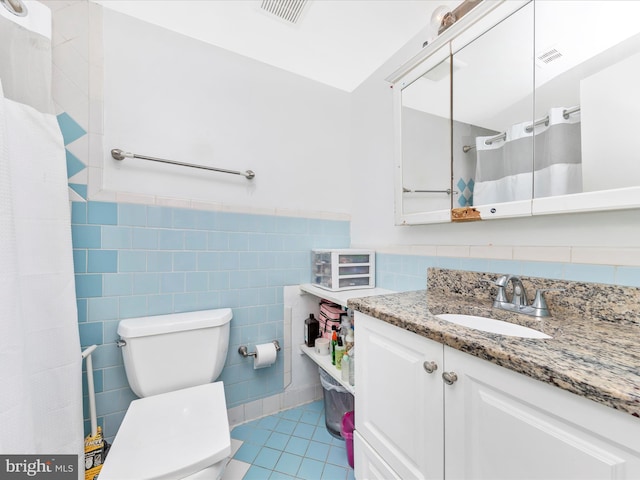 bathroom featuring tile patterned floors, vanity, toilet, and tile walls