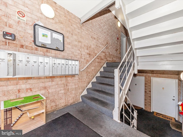 staircase featuring vaulted ceiling with beams, mail boxes, and brick wall