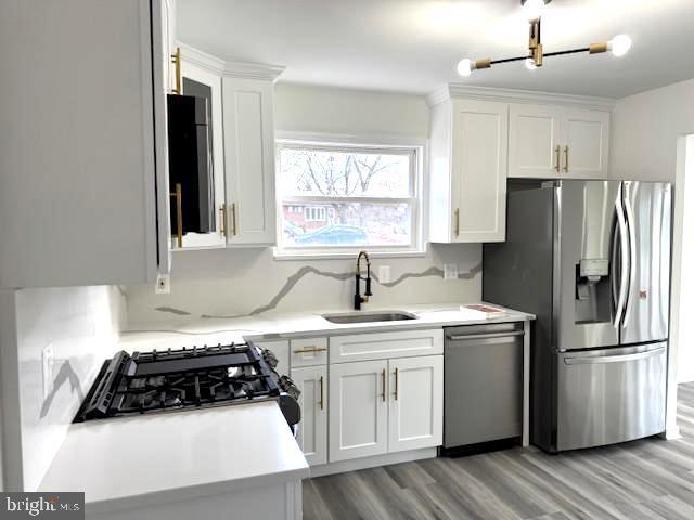 kitchen with tasteful backsplash, stainless steel appliances, sink, light hardwood / wood-style flooring, and white cabinets