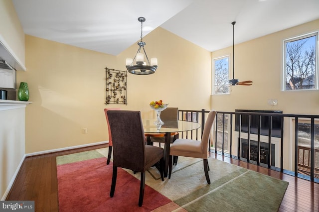 dining space with a healthy amount of sunlight, wood-type flooring, baseboards, and ceiling fan with notable chandelier