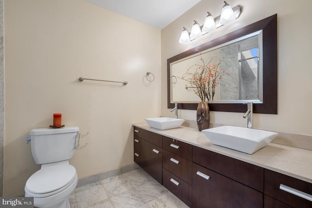 bathroom with toilet, double vanity, baseboards, and a sink