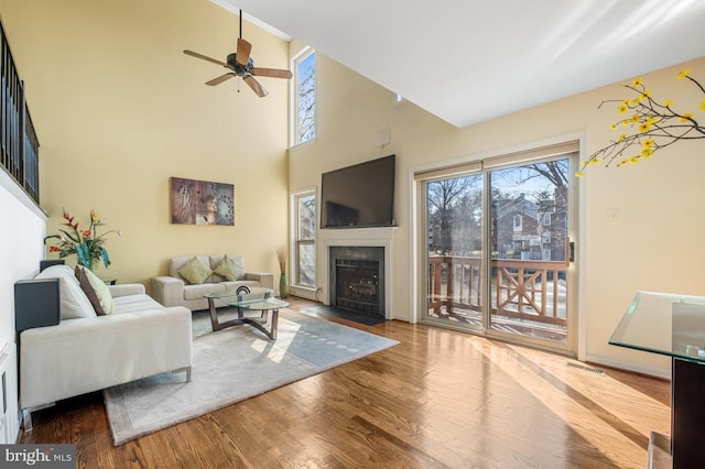 living room with ceiling fan, a high ceiling, a fireplace with flush hearth, wood finished floors, and visible vents