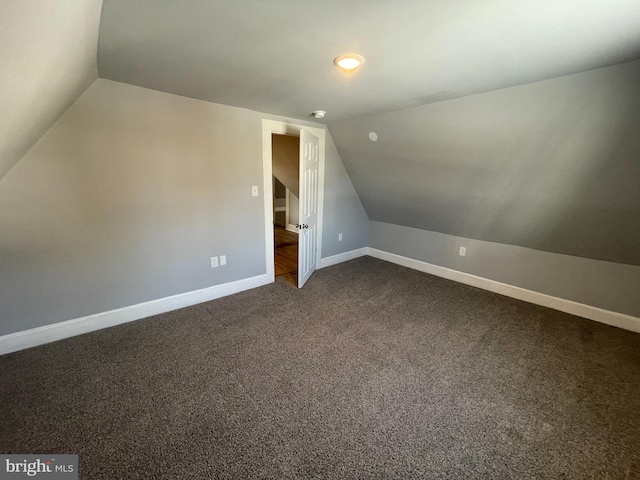 additional living space featuring dark colored carpet and vaulted ceiling